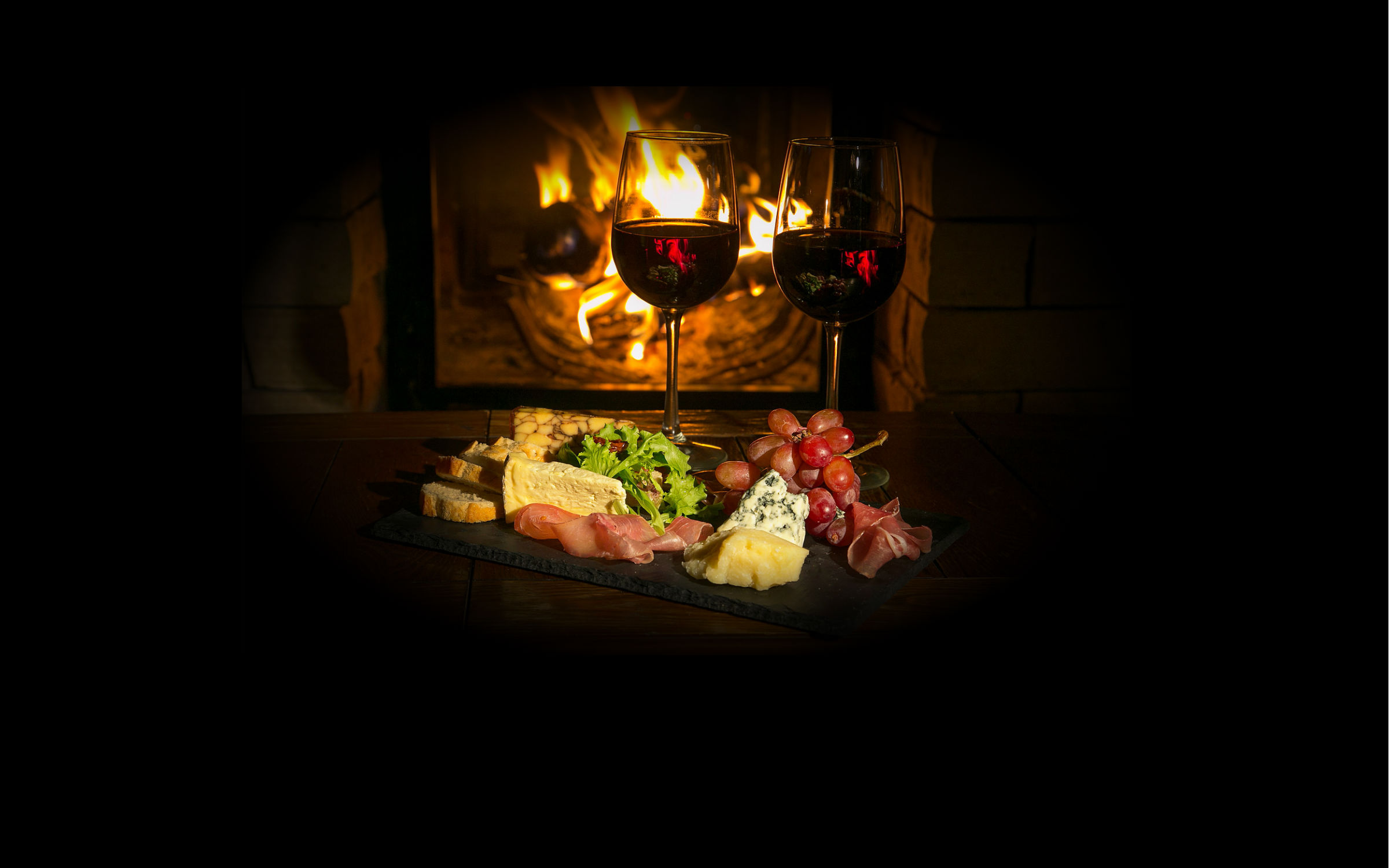 Two glasses of wine sit in front of a fire